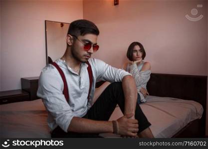 a young swarthy guy and a young brunette girl are sitting on the bed in the bedroom with sad faces. selective focus on the girl