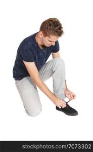A young tall man in jeans kneeling on the floor in the studio tying up hisshoe lace, isolated for white background