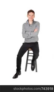 A young teen boy, sitting in a gray sweater with his arms crossed smiling on a chair, isolated for white background