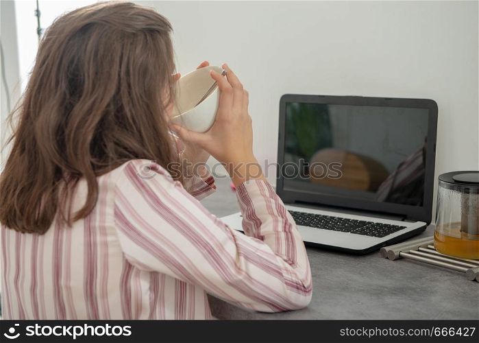a young teenage drinking a cup of tea with a laptop