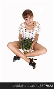A young teenager girl sitting on the floor in shorts and high heels, talkingcare of a small plant, looking into the camera, for white background.