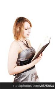 A young teenager girl standing for white background in a silver dressand reading in a black book.