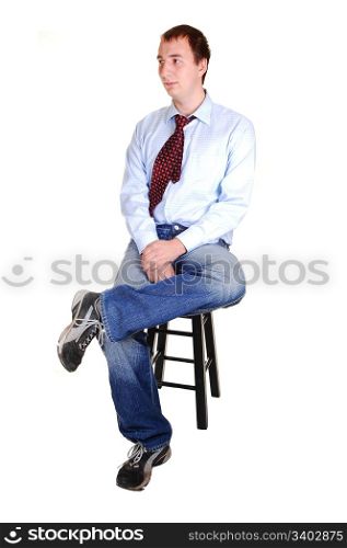 A young teenager in jeans and blue dress shirt with tie sitting on a chair in thestudio for white background isolated.