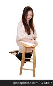 A young teenager kneeling on the floore, in tights and with long brunettehair and a notebook on a chair in front of her, for white background.