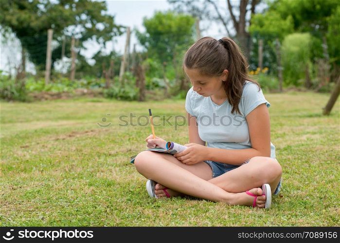 a young teenager sitting and writing cross-legged in the grass