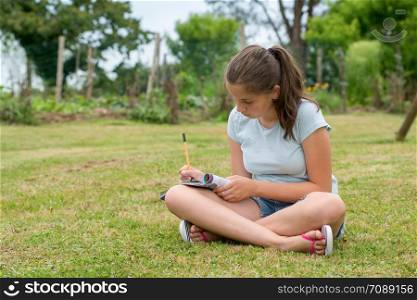 a young teenager sitting and writing cross-legged in the grass