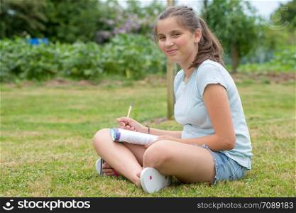 a young teenager sitting cross-legged and writing in the grass