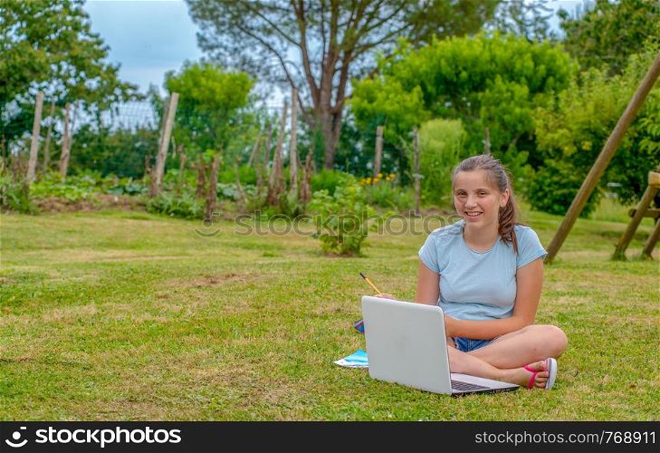 a young teenager sitting in the grass using a laptop