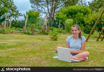 a young teenager sitting in the grass using a laptop