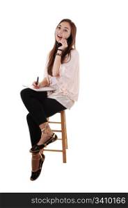 A young teenager sitting on a chair, in black tights and with long brunettehair and a notebook in her hand, on the cell phone, for white background.