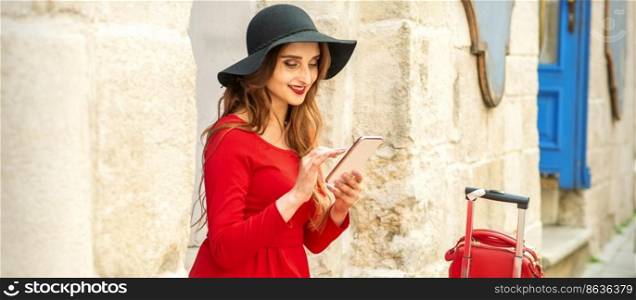 A young traveling white woman in the red jacket and black hat sitting with a smartphone on the city street. A young traveling white woman in the red jacket and black hat sitting with a smartphone on the city street.