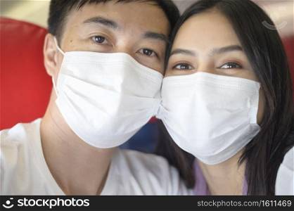 A young travelling couple taking a sefie is wearing protective mask onboard in the aircraft, travel under Covid-19 pandemic, safety travels, social distancing protocol, New normal travel concept