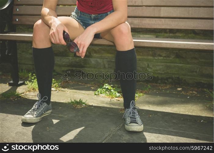 A young trendy woman is relaxing on a park bench on a sunny summer day