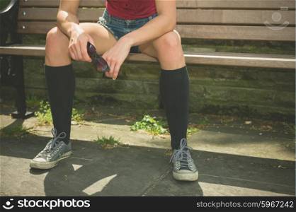 A young trendy woman is relaxing on a park bench on a sunny summer day