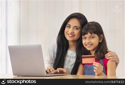 A YOUNG WOMAN AND DAUGHTER LOOKING AT CAMERA WHILE DOING ONLINE TRANSACTION