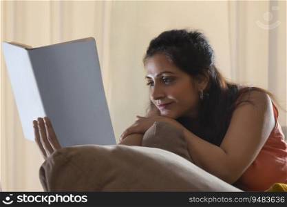 A YOUNG WOMAN COMFORTABLY RESTING ON SOFA AND READING A BOOK