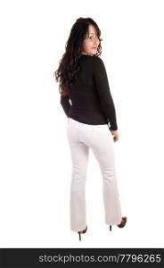 A young woman dressed up in white dress pants and a black sweaterand her long curly black hair standing from the back for white background.