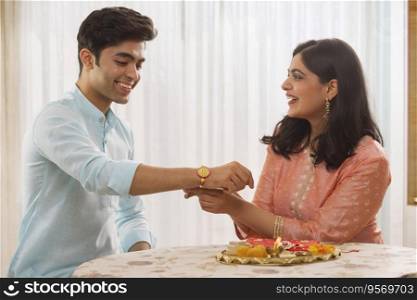 A YOUNG WOMAN HAPPILY TYING RAKHI TO BROTHER