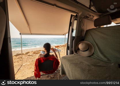 A young woman having breakfast in her caravan observing a good view of the beach