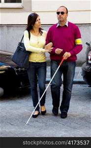 a young woman helps a blind man cross the road