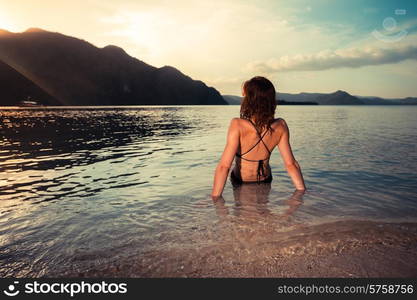 A young woman in a bikini is sitting on a tropical beach at sunset