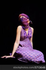 A young woman in a colorful sundress and hijab on black background