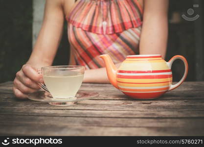 A young woman in a summer dress is drinking tea at a wooden table