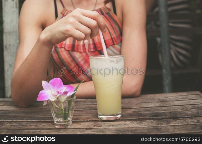 A young woman in a summer dress is drinking tea at a wooden table outside