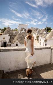 A young woman in a white dress and  hat on a sunny day during tourist visit in Alberobello, Italy