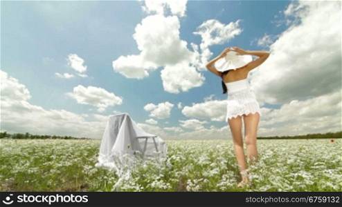 A young woman in a white hat relaxing on a white blossoming meadow looking at the camera