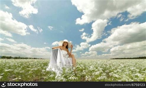 A young woman in a white hat relaxing on a white blossoming meadow
