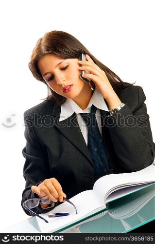 a young woman in black jacket and white shirt and a tie sitting down behind an office table and talking by phone