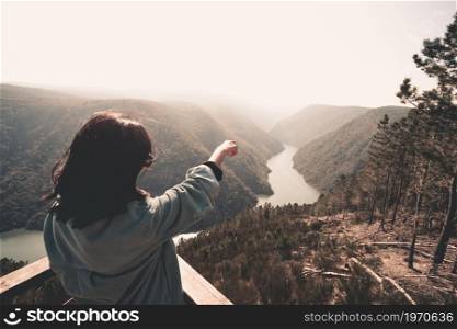 A young woman in front of a massive river pointing to the horizon during a sunny day wellness and liberty concept