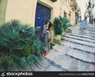 A young woman in long olive dress and hat is standing outside the old retro blue door on big stairs. Vacation and travel time. Malta, La Valetta. A young woman in long olive dress and hat is standing outside the old retro blue door on big stairs. Vacation and travel time.