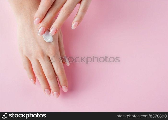 A young woman is applying cream to her hands. Spa and body care concept on pink background. Place for text.. A young woman is applying cream to her hands. Spa and body care concept on a pink background. Image for advertising.