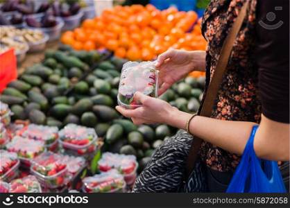 A young woman is at a fruit and vegetable market and is hoding a box of strawberries