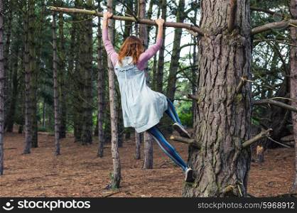 A young woman is climbing a tree in the forest and is hanging from a branch