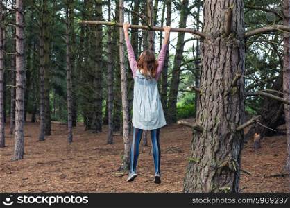 A young woman is climbing a tree in the forest and is hanging from a branch