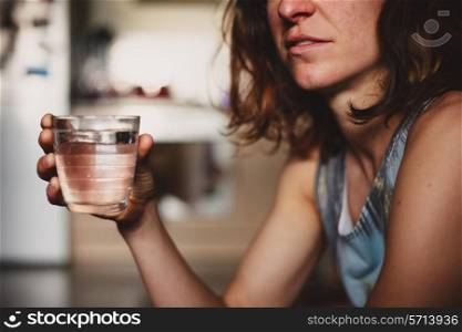 A young woman is drinking a glass of water at home in her kitchen