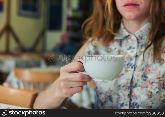 A young woman is drinking coffee in a cafe during the day