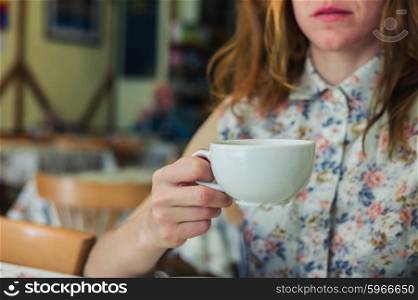 A young woman is drinking coffee in a cafe during the day