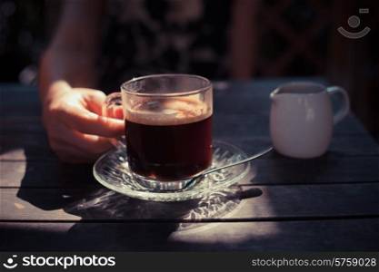 A young woman is drinking coffee outside in the sunlight
