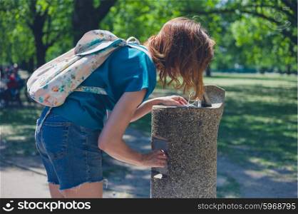 A young woman is drinking from a water fountain in a park on a sunny day in the summer