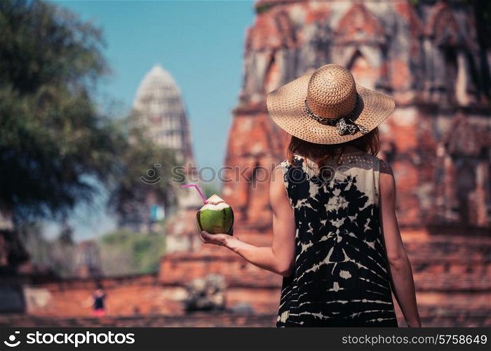 A young woman is drinking juice from a coconut near the ruins of an ancient buddhist temple