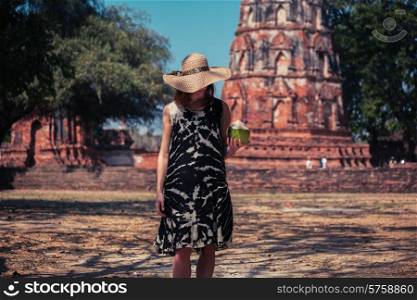 A young woman is drinking juice from a coconut near the ruins of an ancient buddhist temple