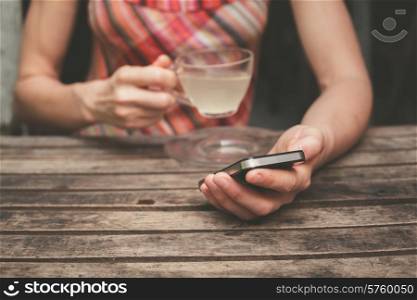 A young woman is drinking tea and using her smart phone at a wooden table