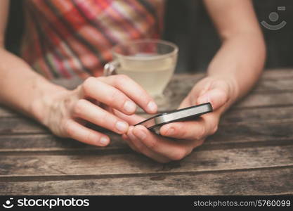 A young woman is drinking tea and using her smart phone at a wooden table