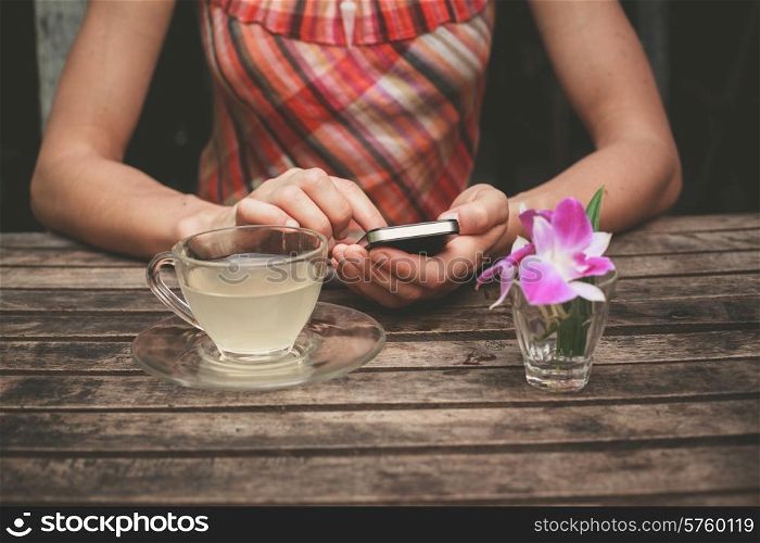 A young woman is drinking tea and using her smart phone at a wooden table