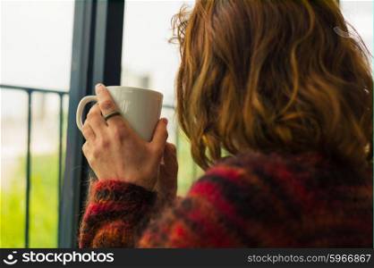 A young woman is drinking tea by a window
