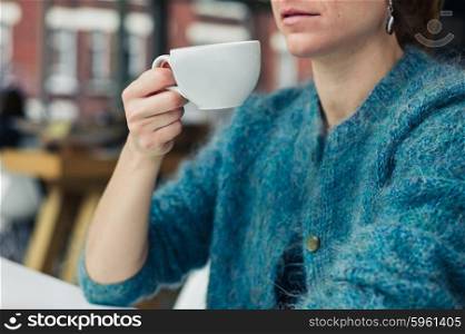 A young woman is drinking tea or coffee from a cup in a caffe